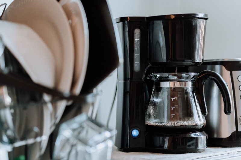 Une cafetière est posée sur le comptoir, remplie de café, derrière un support de vaisselle propre.