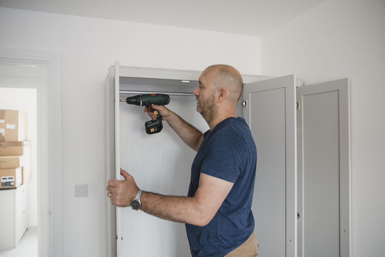 Un homme mûr construit une armoire dans la chambre de sa nouvelle maison.