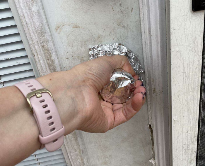 Une main saisit une poignée de porte recouverte d'une feuille d'aluminium.