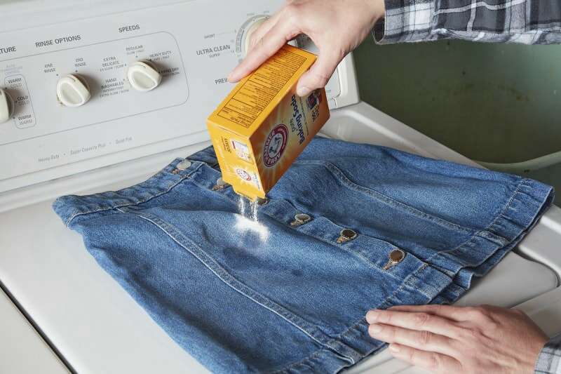 Une femme saupoudre du bicarbonate de soude sur une jupe en jean tachée.