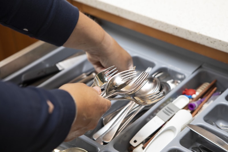 iStock-1329464289 procrastination hacks Gros plan sur les mains d'une femme qui range des fourchettes et des cuillères dans un tiroir à couverts.