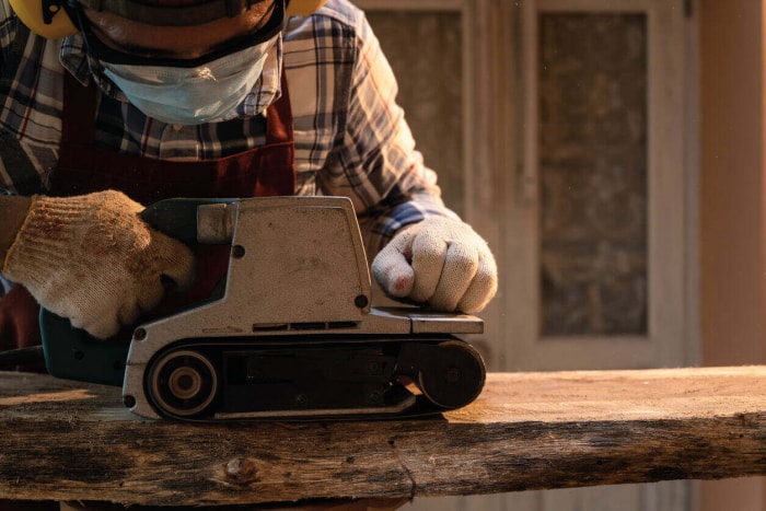 Les charpentiers utilisent une ponceuse à bande électrique portative pour niveler la surface du bois dans l'atelier de menuiserie.