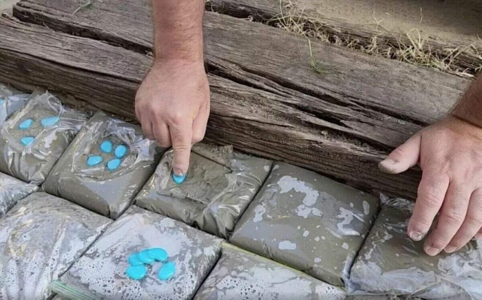 Personne plaçant des pierres bleues sur du béton humide exposé dans des sacs en plastique.