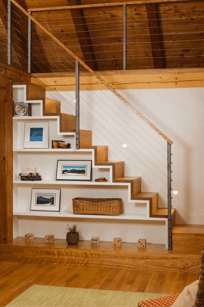 escalier en bois clair menant au grenier avec plafonds en poutres de bois et étagères sous l'escalier présentant des œuvres d'art encadrées