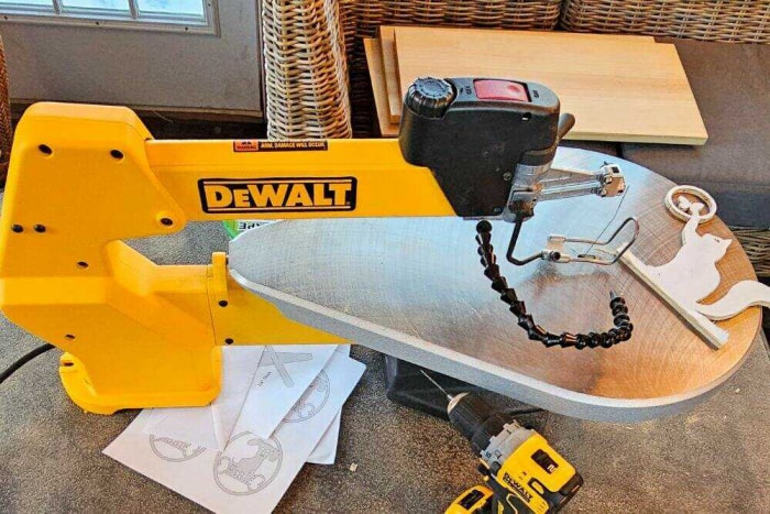 La scie à chantourner DeWalt sur un établi avec un objet de décoration en bois récemment coupé, des pochoirs en papier, des dalles de bois non coupées et une perceuse DeWalt.