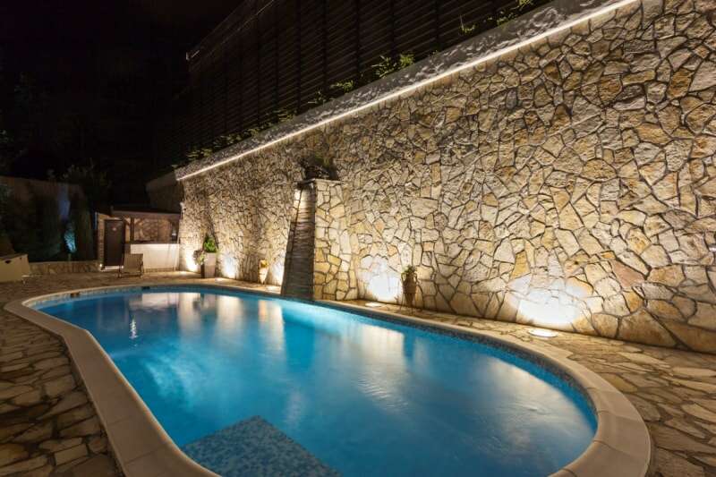 Une piscine avec des lumières encastrées dans la terrasse en pierre. 