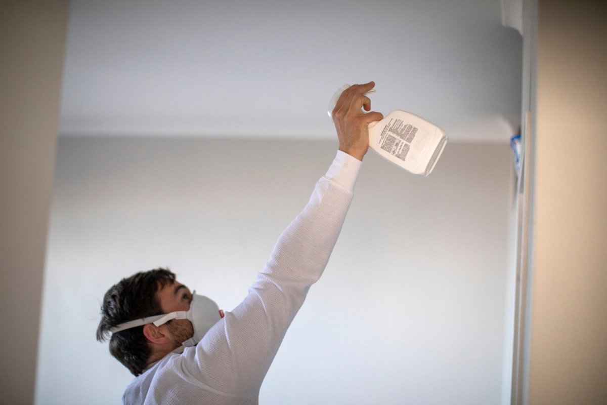 Une personne pulvérise une solution sur un mur tout en portant un masque de protection.