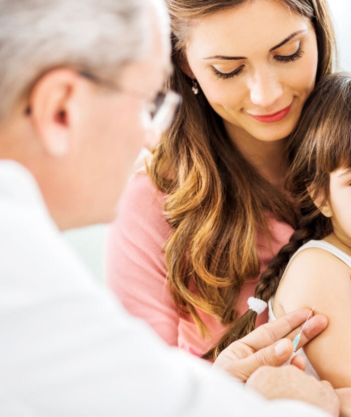 Jeune fille avec ses parents se faisant vacciner par un médecin qui pointe l'aiguille sur son bras