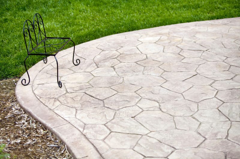 Partie d'un patio en béton matricé arrondi avec une chaise en fer à côté d'une pelouse bien entretenue.