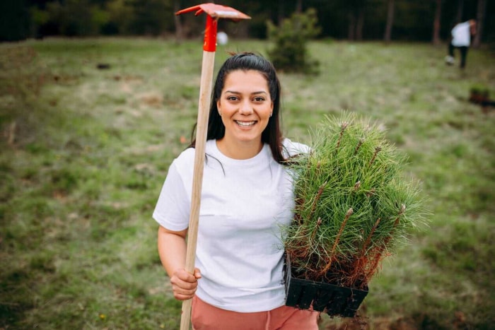 Jeune femme tenant une houe et des jeunes arbres