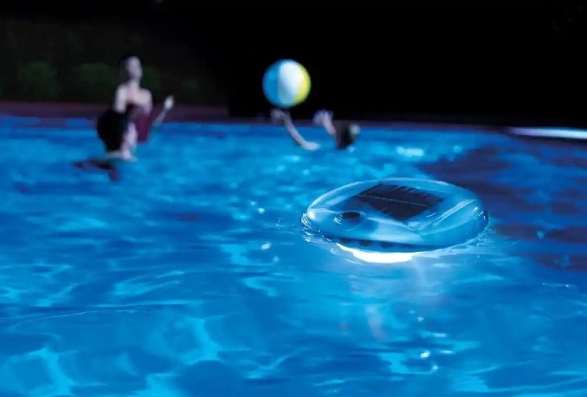 Les gens jouent dans la piscine la nuit avec une lumière de piscine flottante.