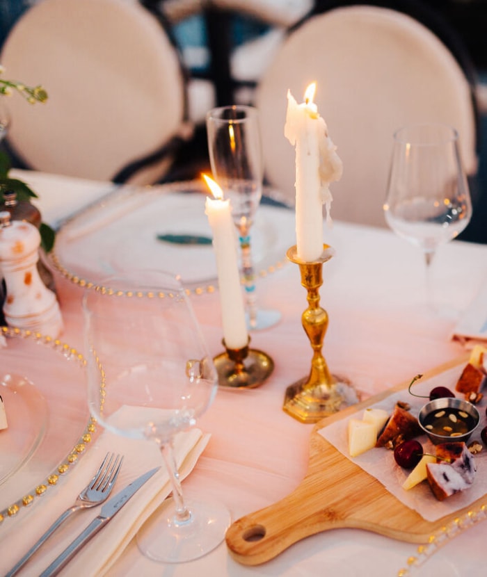 Table décorée d'assiettes avec des perles et des bougies sur une nappe blanche et des cerises et du fromage sur une planche à découper.