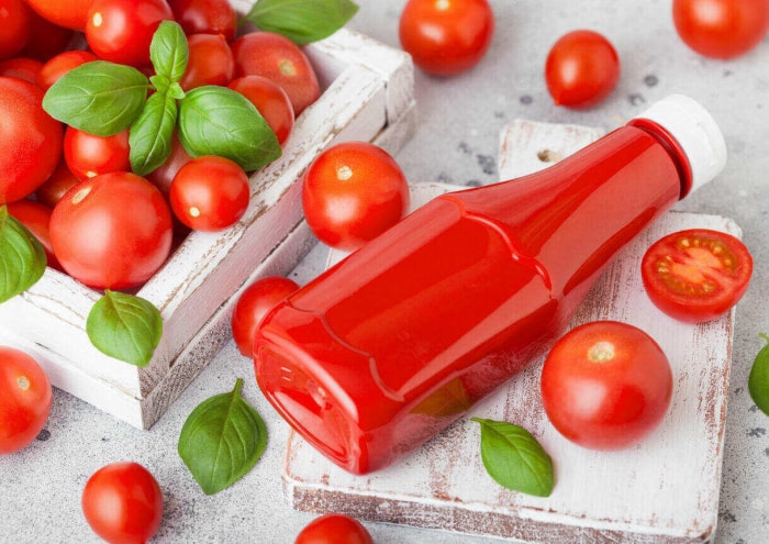 Bouteille de ketchup sans étiquette à côté de plusieurs tomates cerises fraîches