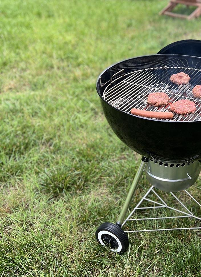 Le barbecue au charbon de bois Weber Original Kettle Premium en cours d'utilisation pour griller de la viande dans une cour