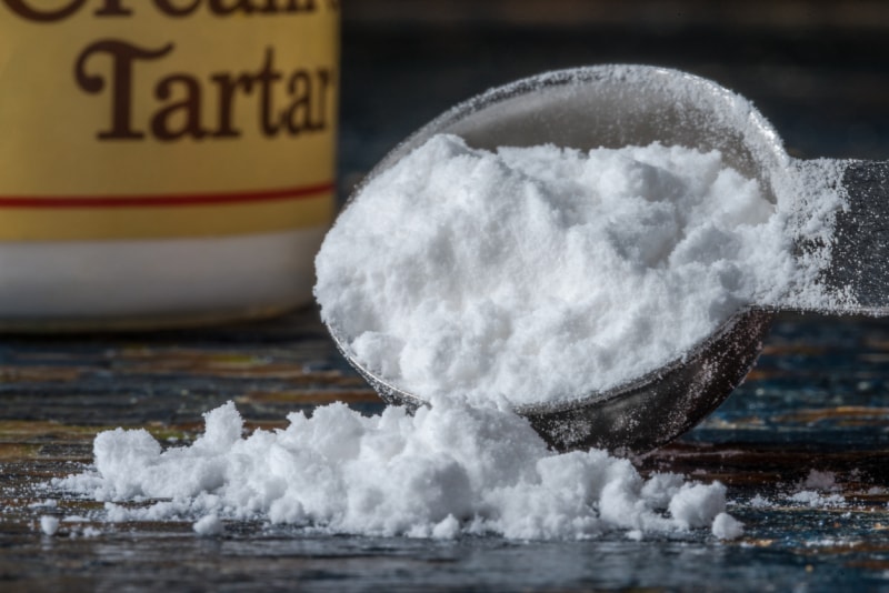 Crème de tartre débordant d'une cuillère à soupe avec un pot de crème de tartre en arrière-plan