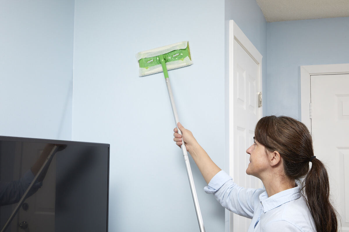 Une femme utilise un Swiffer pour dépoussiérer les murs de sa maison.