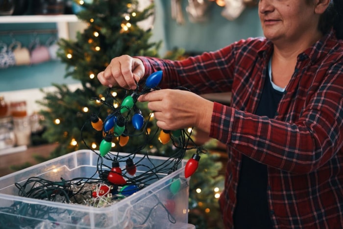 Une femme démêle des guirlandes de Noël dans une boîte.