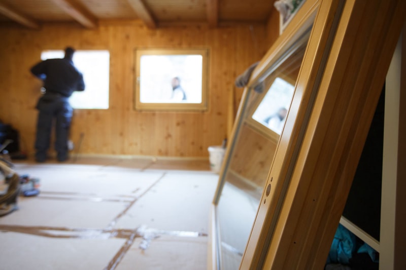 Une fenêtre est posée au sol au premier plan, attendant d'être installée par un ouvrier habillé de bleu en arrière-plan.