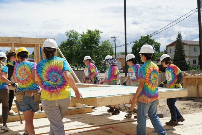 Un groupe de bénévoles du Pride Month Metro Denver transporte un cadre mural terminé sur un chantier.