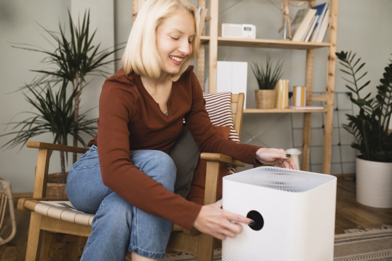 Une femme allume son purificateur d’air alors qu’elle est assise dans son salon.