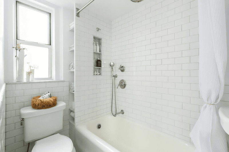 Une salle de bain exiguë avec une baignoire-douche combinée, des toilettes et des étagères très étroites du sol au plafond.