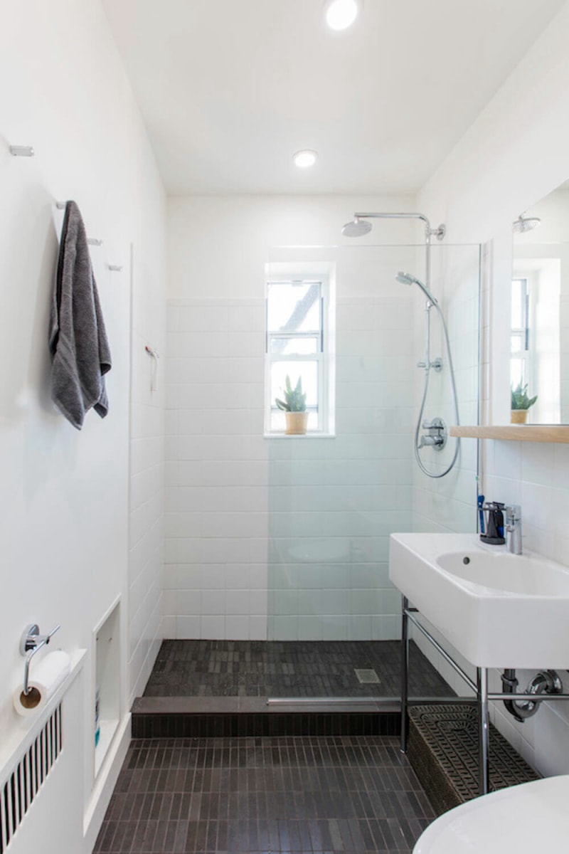 Une salle de bain étroite de style salle d'eau avec des murs en carrelage blanc et un sol en ardoise foncé.