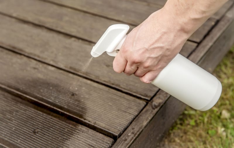 Mélange de répulsif à fourmis fait maison en spray dans une bouteille. Une personne pulvérise à la main un insectifuge sur les planches de bois de la terrasse de sa maison.