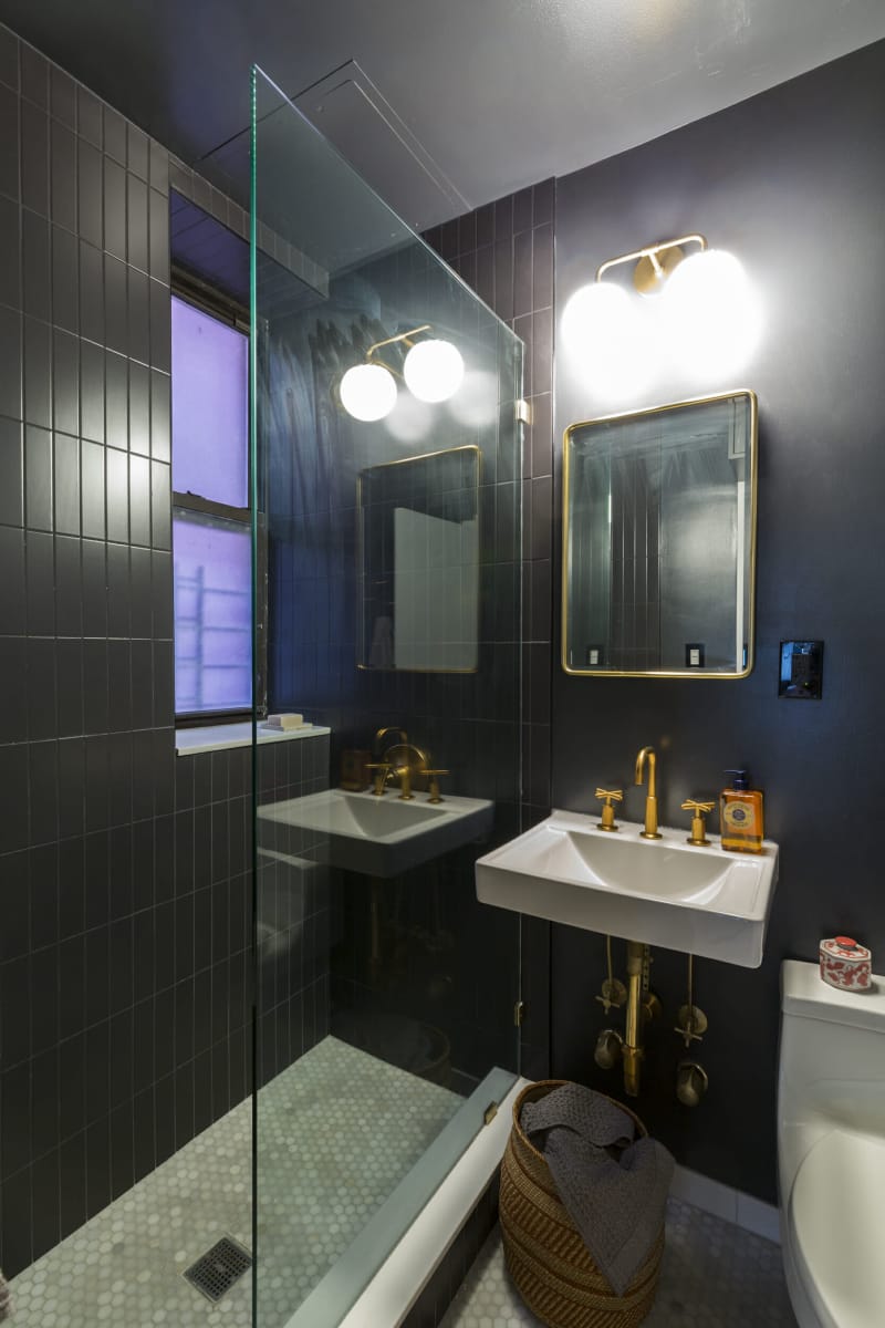 Une petite salle de bain avec des murs noirs et un lavabo, une douche et des luminaires dorés.