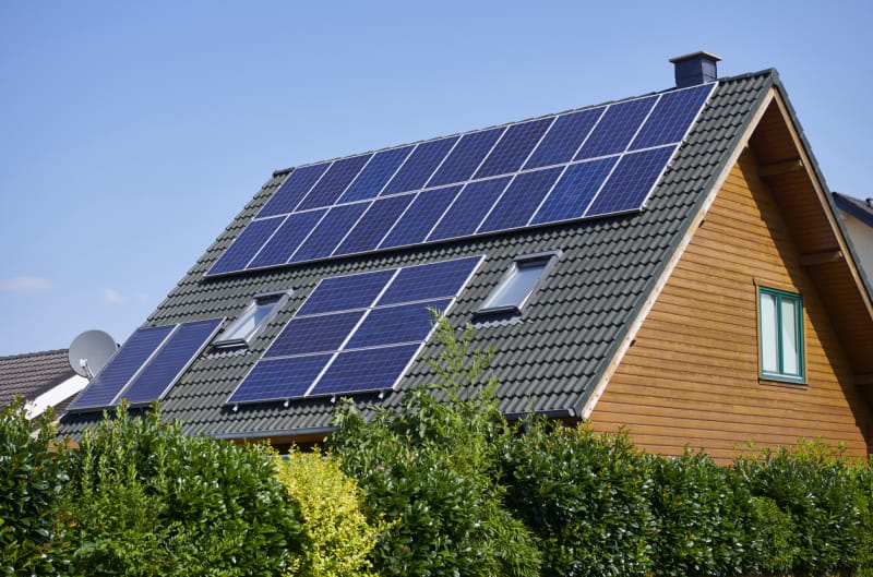 Une maison en bois avec des panneaux solaires le long du toit en tuiles noires.