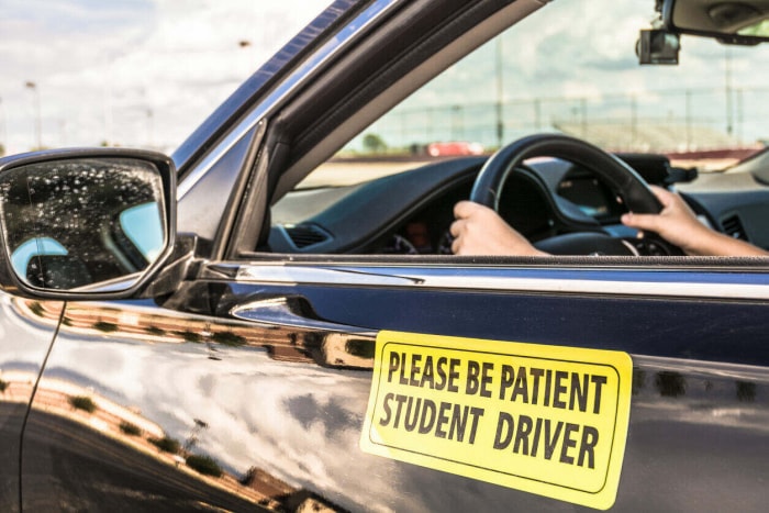 vue rapprochée du côté conducteur du véhicule avec le panneau "please be patient student driver" (soyez patient, élève conducteur)