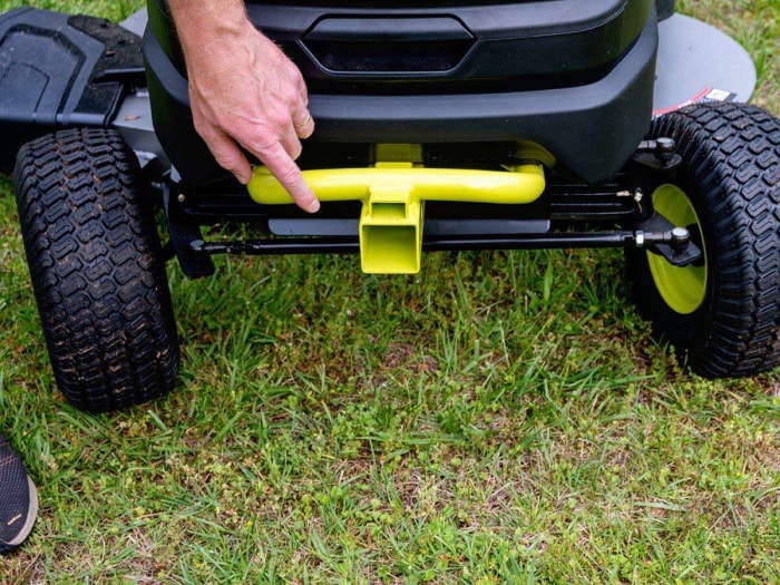 Main d'une personne sur l'attelage d'un tracteur de pelouse Ryobi jaune