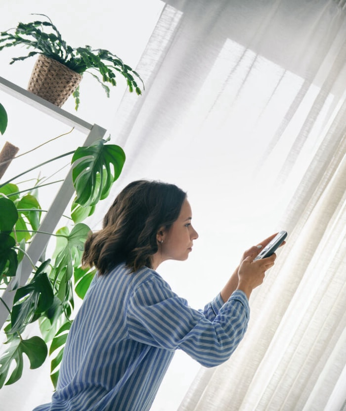 jeune femme utilisant une télécommande pour faire fonctionner le climatiseur monté en hauteur sur le mur dans un salon lumineux et aéré