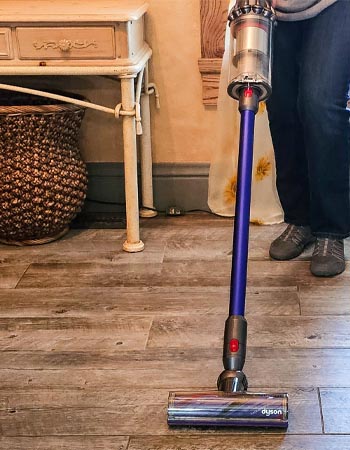 Personne passant l'aspirateur sur un sol en bois avec l'aspirateur-balai sans fil Dyson V11 Animal