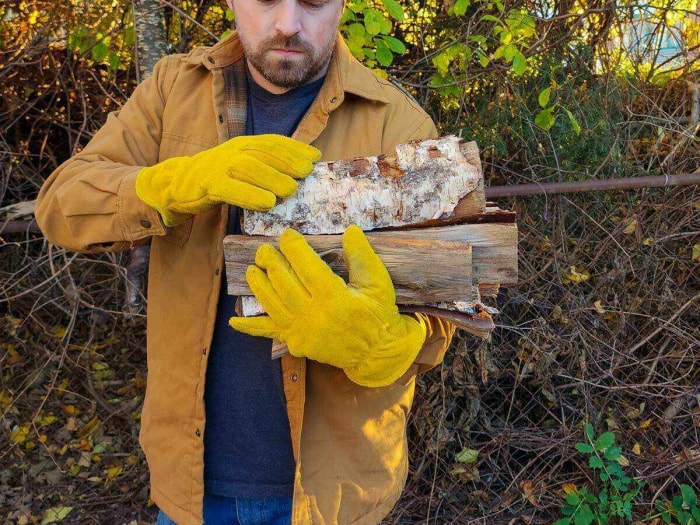 Une personne portant les meilleurs gants de travail d’hiver tout en ramassant du bois de chauffage à l’extérieur.