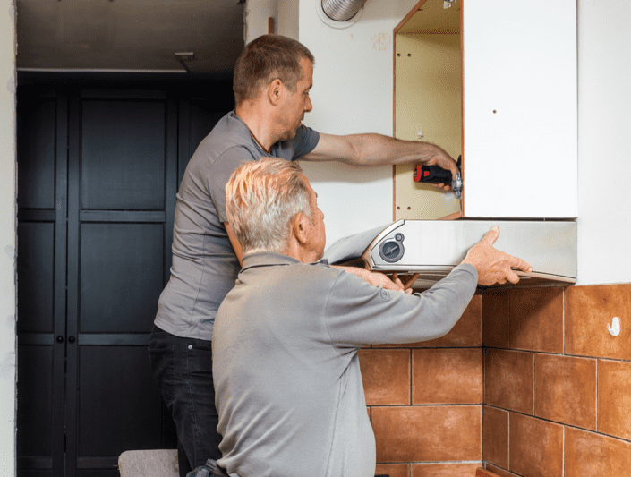 un homme aide un homme plus âgé à retirer la hotte de cuisine et l'armoire pour une élimination responsable lors d'une rénovation durable de la cuisine