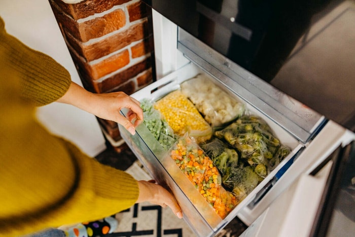 femme ouvrant un congélateur rempli de légumes