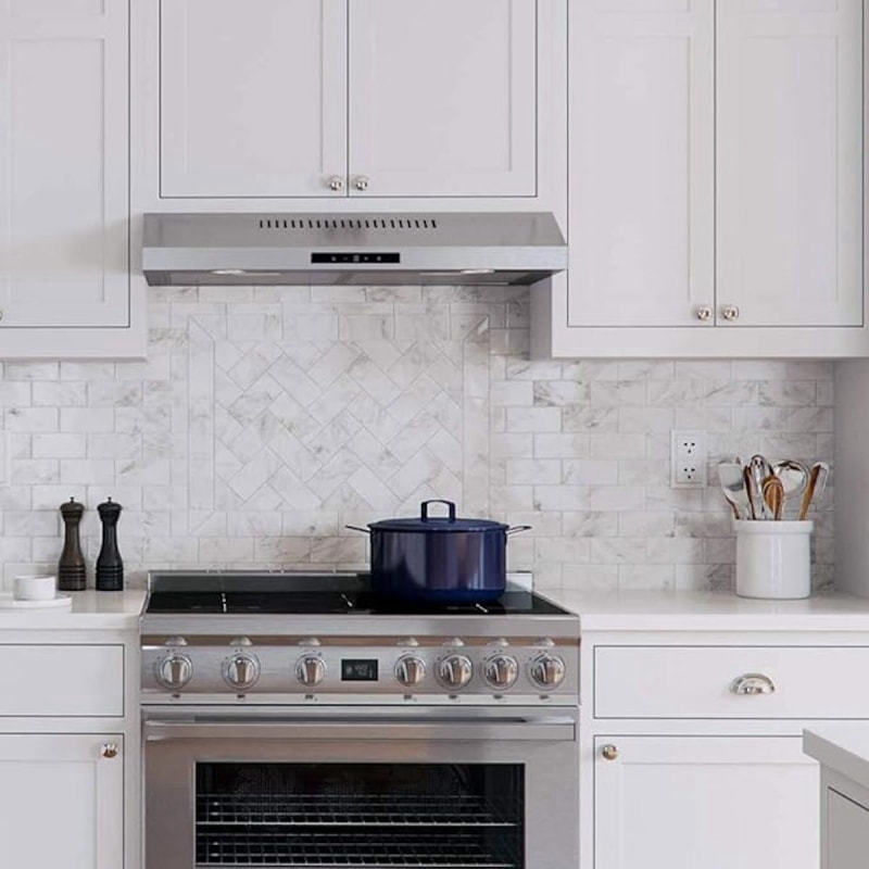 Une hotte de cuisinière encastrée dans une cuisine blanche avec une casserole bleue sur la cuisinière.